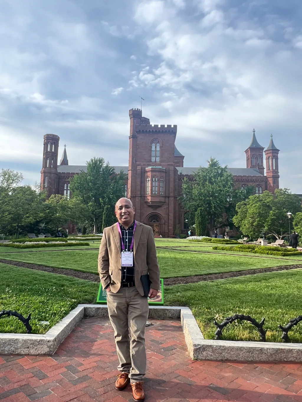 Outdoor portrait on a garden path in front of a historic red sandstone castle building.